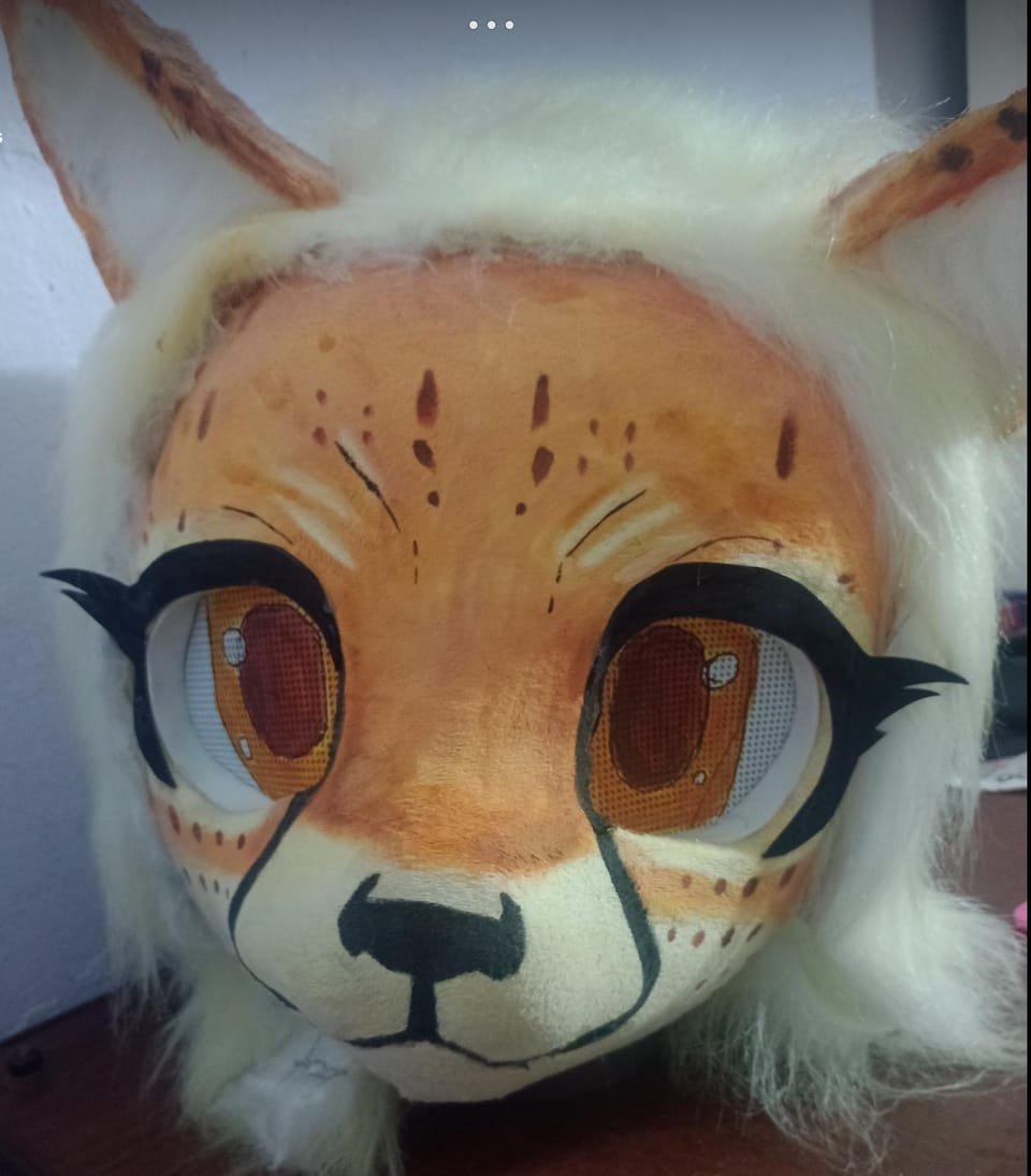 Cabeza de fursuit crema y naranja tipo zorro, primer plano frontal con ojos grandes estilo anime.