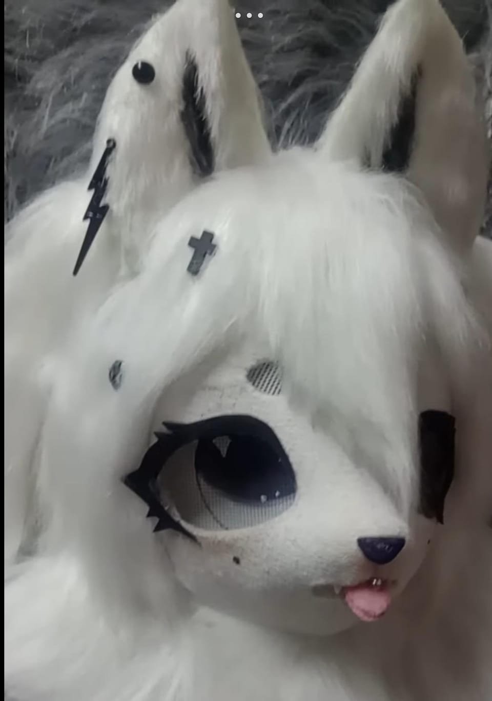 Cabeza de fursuit blanca con manchas negras tipo husky, ojo grande visible y lengua afuera.