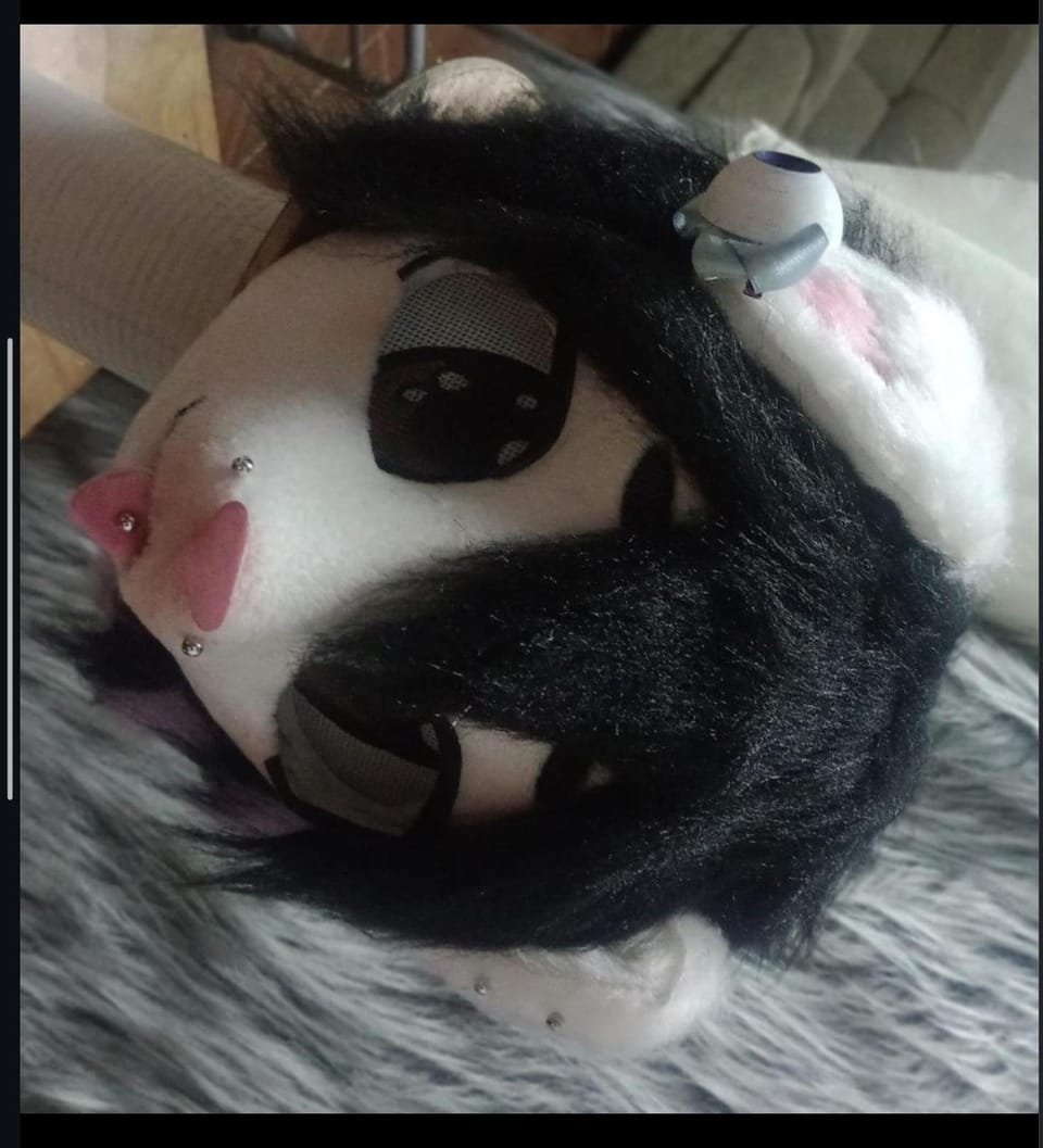 Cabeza estilo kigurumi con peluca oscura, rostro blanco y detalles decorativos.