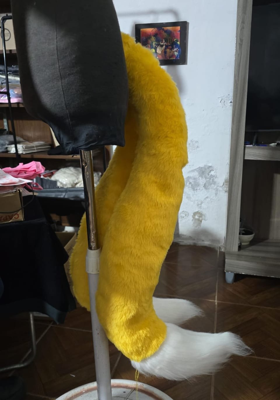 Cola de fursuit amarilla con punta blanca sobre soporte.