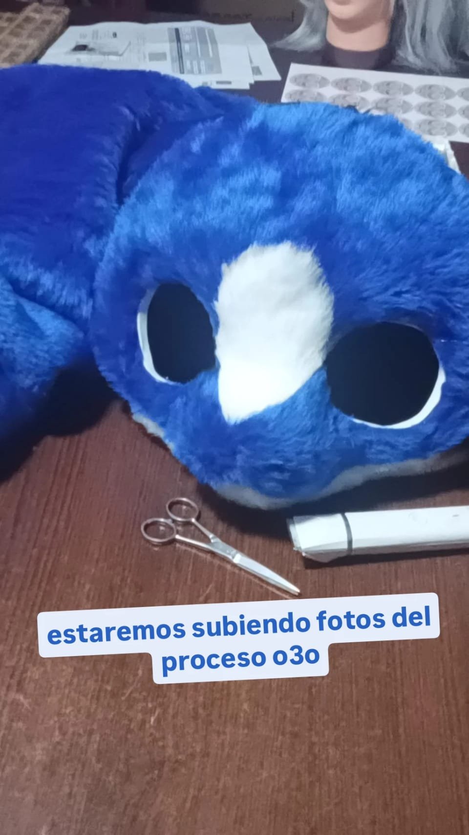 Cabeza de fursuit azul en proceso, sin ojos colocados, con referencias de diseño cerca.