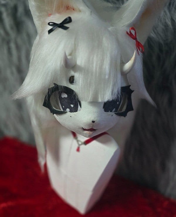 Cabeza de fursuit blanca tipo zorro espiritual con cuernos, moños decorativos y detalles pintados en el rostro, vista frontal.