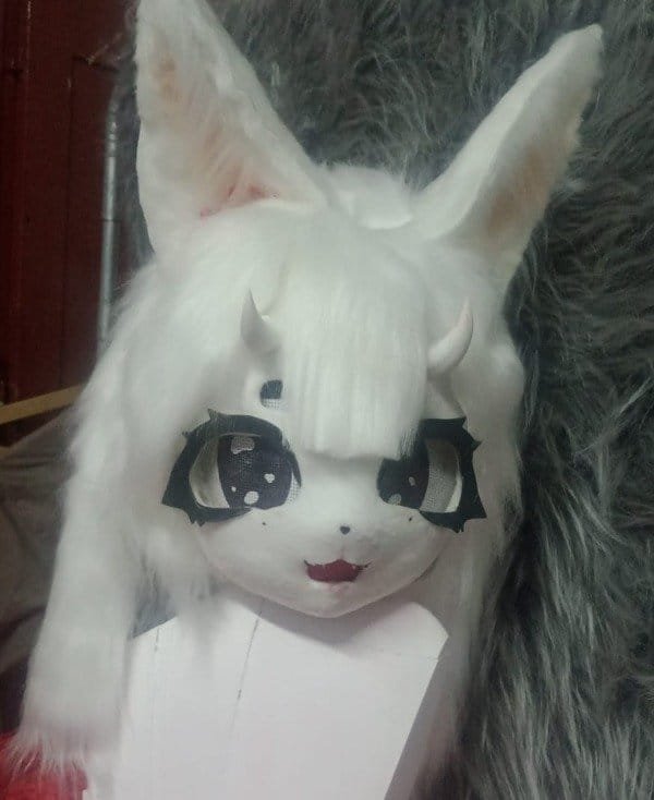 Cabeza de fursuit blanca tipo zorro espiritual, vista de tres cuartos mostrando el pelaje suave y los cuernos.